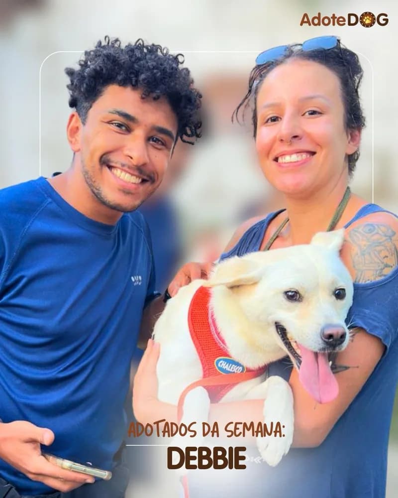 Debbie, cadela branca de colete, no colo da família que a adotou